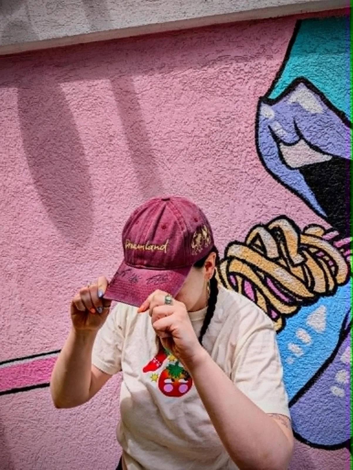 Person wearing the signed Dreamland Cafe hat in front of a colourful street mural
